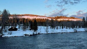 En stuga vid en flod med snötäckta stränder och träd.