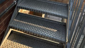 Un ensemble d’escaliers en métal, dotés d’une surface texturée, menant à une plateforme en bois.