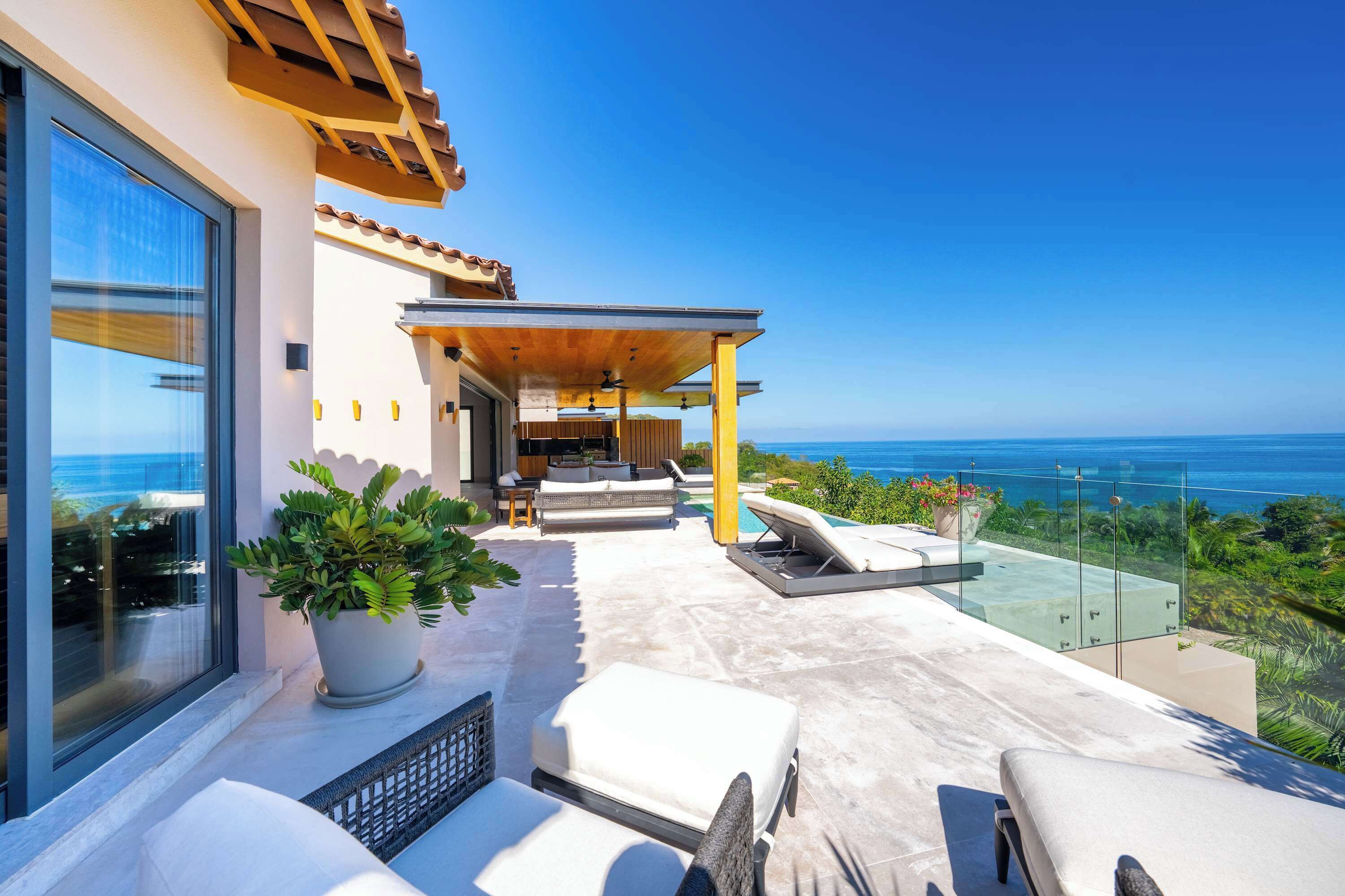 A modern outdoor patio with a view of the ocean, featuring a seating area with cushions and a potted plant.