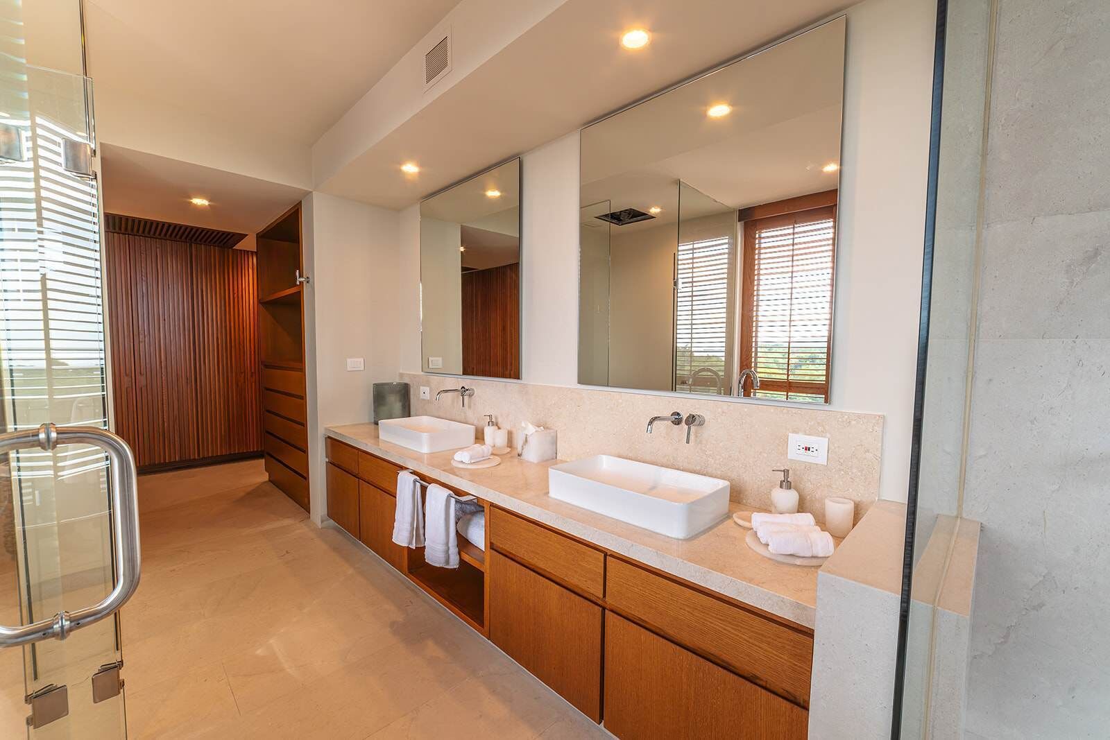 Un baño moderno con un espejo grande, dos lavamanos, armarios de madera y una cabina de ducha de vidrio.