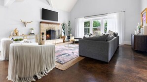 Ein geräumiges Wohnzimmer mit Kamin, einem grauen Sofa und einem großen Fenster.
