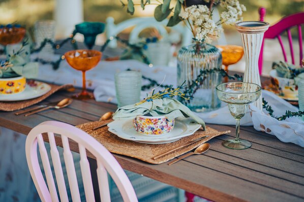 Une table dressée avec différents plats et de la verrerie, entourée de chaises et d’éléments décoratifs.