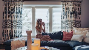 Ein gemütliches Wohnzimmer mit großem Fenster, gemusterten Vorhängen, einer Couch mit Kissen und einem Couchtisch mit Kerzen.