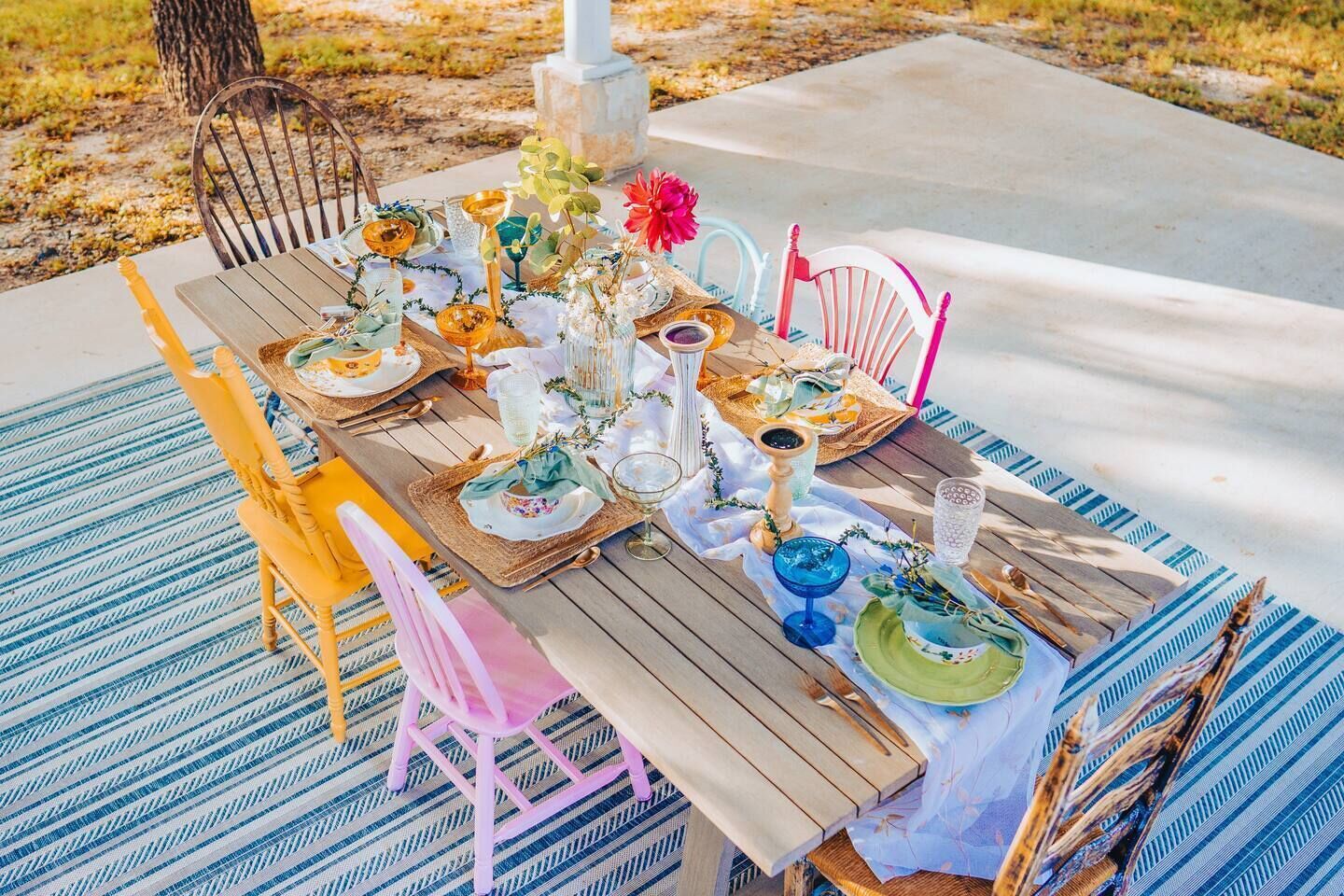 Une table de jardin, dressée pour un repas en plein air, avec des assiettes, des verres et des objets décoratifs.