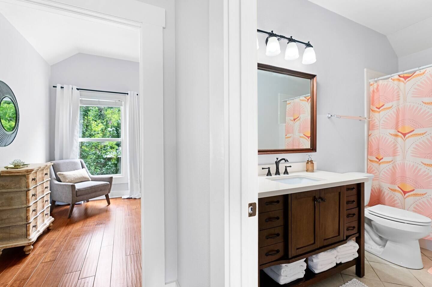 A modern bathroom with a vanity, sink, and toilet. There is a window with a view of greenery outside.