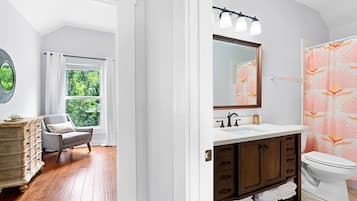 A modern bathroom with a vanity, sink, and toilet. There is a window with a view of greenery outside.