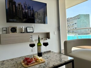 A modern room with a cityscape view, a television, a wine bottle, glasses, and a cheese board. - Paddle y Relax Baia Kristal Con Vista Laguna (Cartagena de Indias)