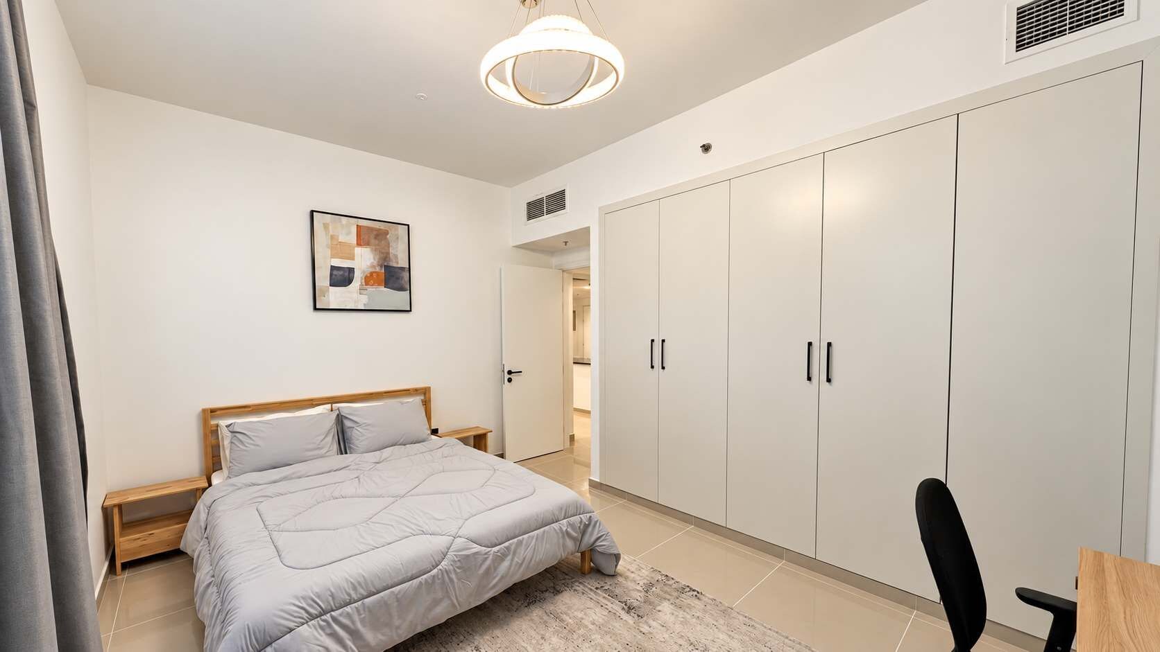 A bedroom with a bed, bedside table, wardrobe, and a painting on the wall.