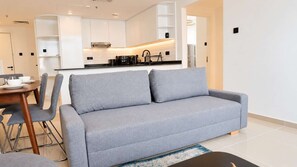 Un salon moderne avec un canapé gris, une table à manger avec des chaises, et une cuisine en arrière-plan.