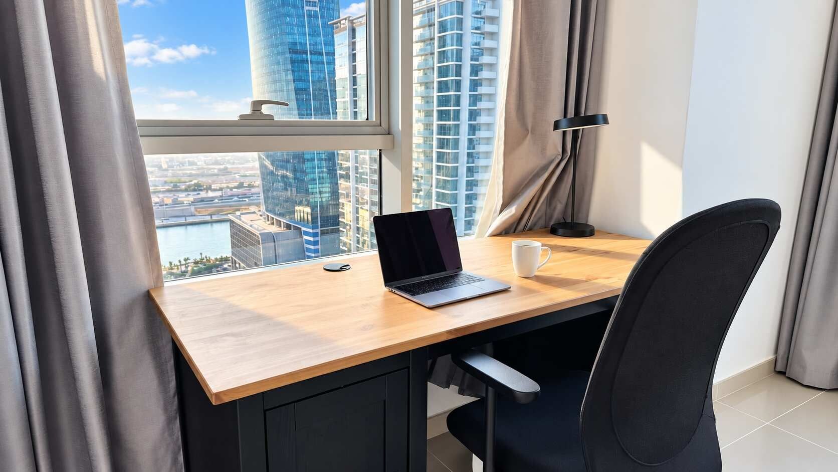 A modern workspace with a laptop, a cup, and a desk by a window overlooking a cityscape.