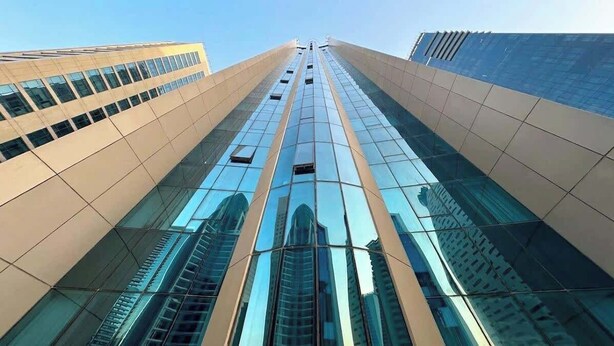 Un immeuble moderne et imposant, doté de grandes fenêtres en verre réfléchissant et d’une façade symétrique.