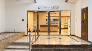L’entrée d’un hôtel, avec une enseigne indiquant « RÉSIDENCE », un sol en marbre et un escalier en métal.