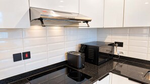 Une cuisine moderne dotée d’un four à micro-ondes, d’un grille-pain et d’une machine à café intégrés, le tout installé sur un plan de travail noir.