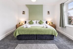 A hotel room with a bed, two bedside tables, a window with curtains, and a green accent wall. - Spacious 4 Bed Home | Free Parking & Fast WiFi (Denton)