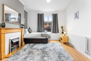 A modern bedroom with a bed, a fireplace, a window with curtains, and a radiator. - Spacious 4 Bed Home | Free Parking & Fast WiFi (Denton)