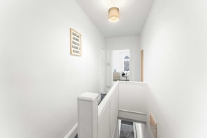 A clean, white hallway with a staircase leading to a room. A framed inspirational quote is visible on the wall. - Spacious 4 Bed Home | Free Parking & Fast WiFi (Denton)