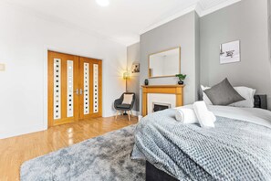 A bedroom with a bed, a chair, a fireplace, and a door with a mirror. - Spacious 4 Bed Home | Free Parking & Fast WiFi (Denton)