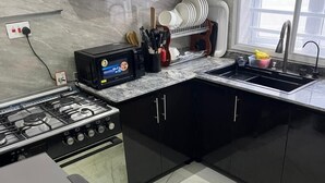 A modern kitchen with black cabinets, a gas stove, a built-in oven, and a microwave. There is a sink with a faucet and a window above it. - Fadaka Manor  (Ibadan)