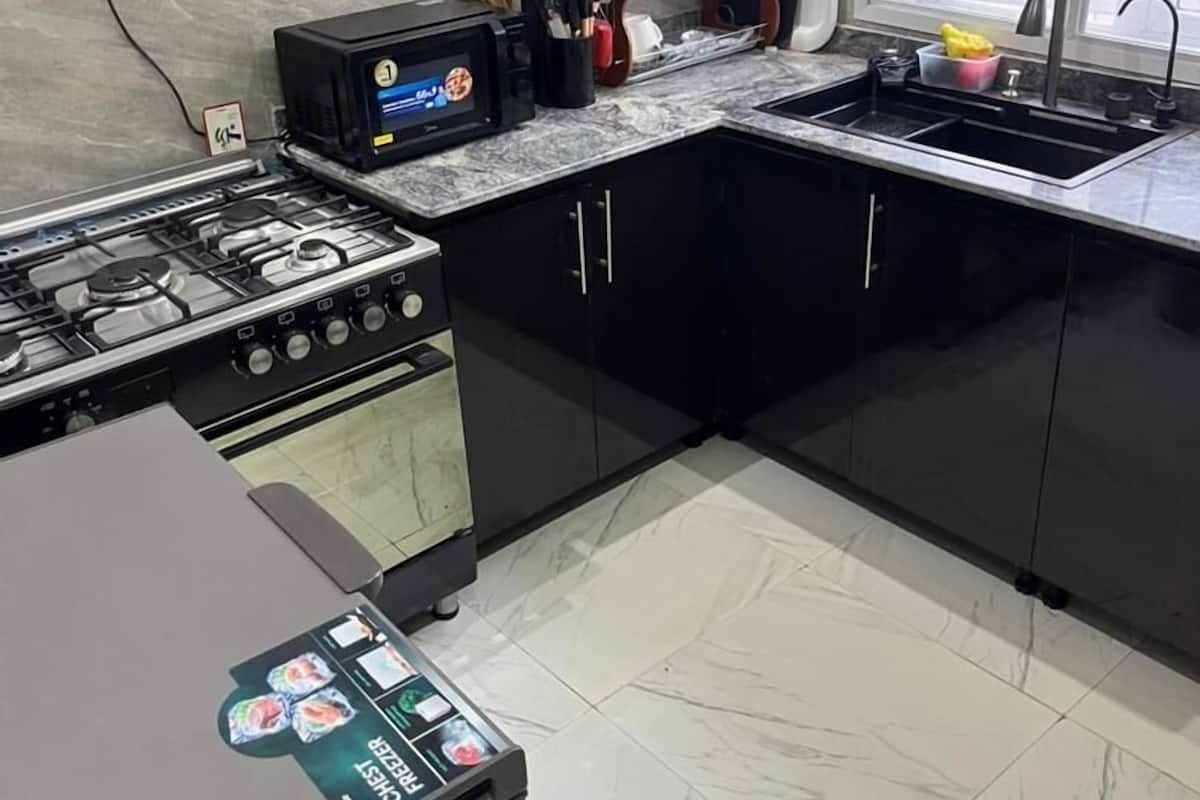 Cocina moderna con armarios negros, estufa a gas, horno empotrado y microondas. Hay un lavamanos con grifo y una ventana arriba.