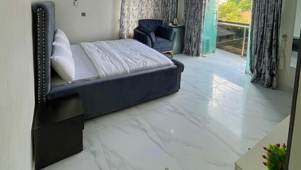 Ein modernes Schlafzimmer mit einem großen Bett, einer Sitzecke und einem Balkon mit Vorhängen.