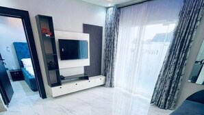 Ein modernes Wohnzimmer mit Flachbildfernseher, einer Couch und einem großen Fenster mit Vorhängen.