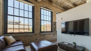 Een moderne woonkamer met een leren bank, een voetenbankje en een grote flatscreen-televisie aan de muur.