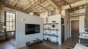 Een moderne woonkamer met een grote flatscreen-tv, een houten plafond en een keukenhoek met roestvrijstalen apparatuur.