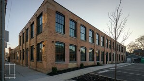 A multi-story brick building with large windows and a parking lot in front. - Industrial Boho Flat - Short North (Columbus)