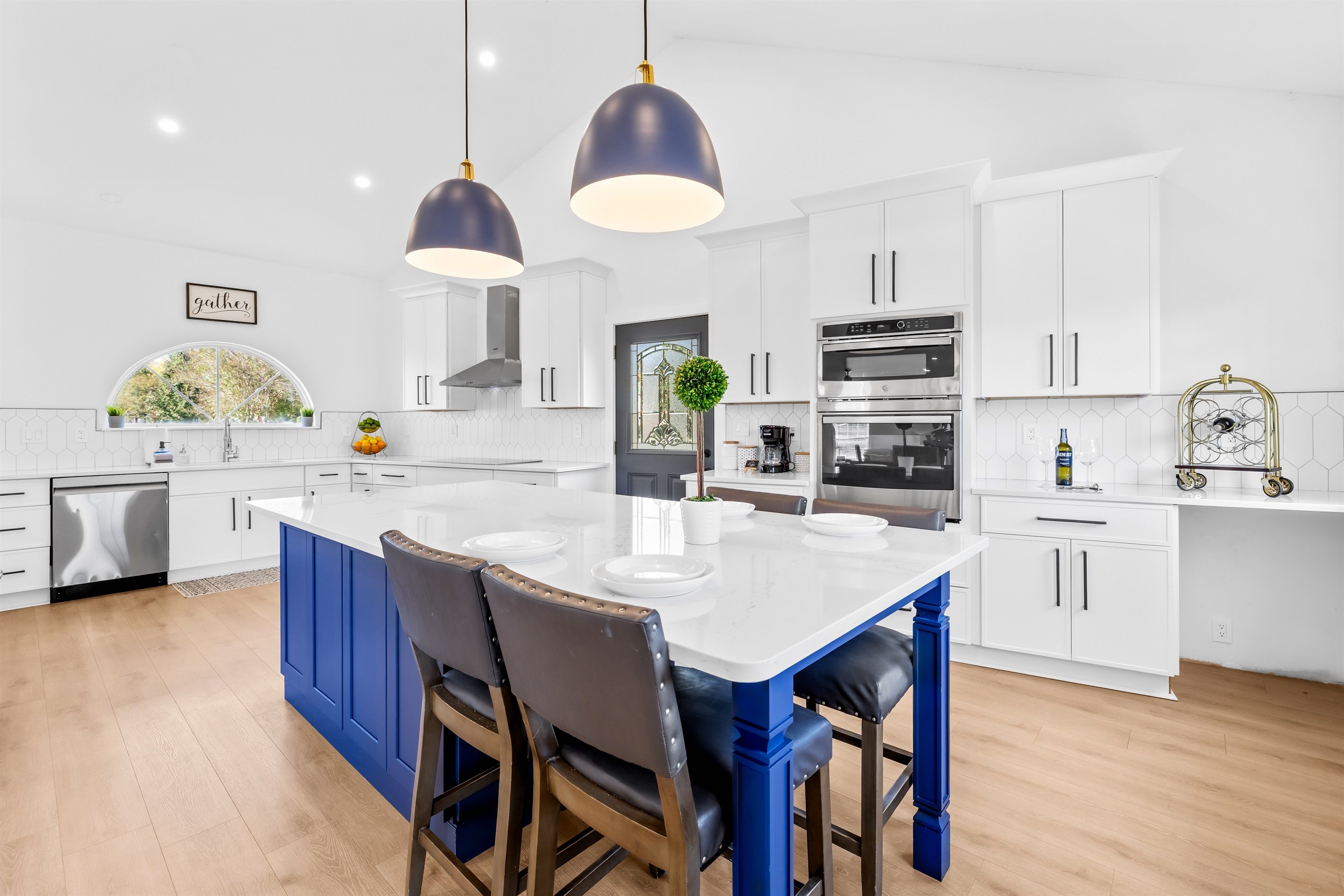 A modern kitchen with white cabinets, a central island, blue bar stools, and pendant lighting.