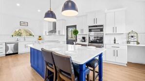 A modern kitchen with white cabinets, a central island, blue bar stools, and pendant lighting. - Lake Access, Game Room, Sleeps 18, Modern! (Mooresville)