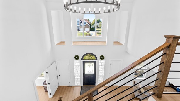 A spacious room with a wooden staircase, a chandelier, and a view of the outside. - Lake Access, Game Room, Sleeps 18, Modern! (Mooresville)