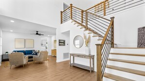 A spacious living room with a wooden staircase, a blue sofa, and a console table. - Lake Access, Game Room, Sleeps 18, Modern! (Mooresville)