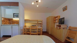 Ein kompaktes Zimmer mit Etagenbett, einer kleinen Küchenzeile, einem Schreibtisch mit Stuhl, einem Fernseher und Holzschränken.