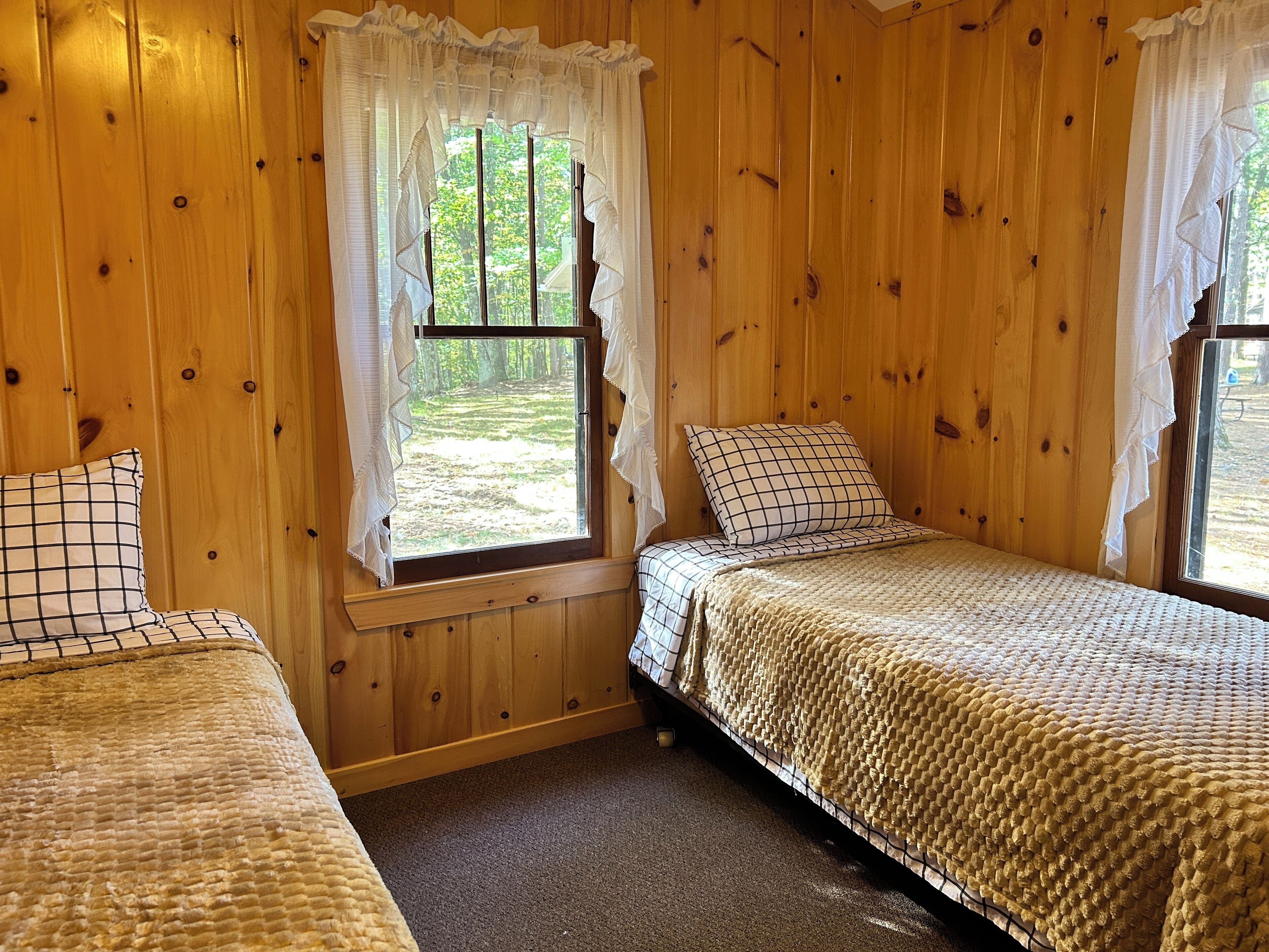 Una cabaña con dos camas de madera, cada una con un cojín a cuadros y una manta tejida.
