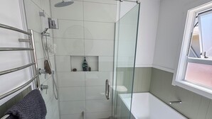Une salle de bain moderne avec une douche à parois de verre, une baignoire blanche et un porte-serviettes avec des serviettes pliées.