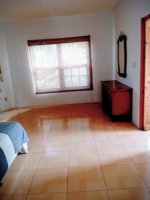 Ein Zimmer mit großem Fenster, einem hölzernen Schminktisch und einem Bett.