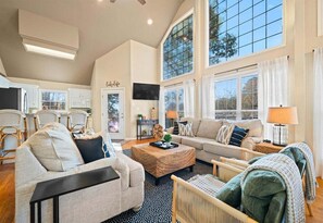 A spacious living room with a high ceiling, large windows, and a cozy seating area with a sofa and chairs. - Peaceful Lakeside Escape with Dock & Hot Tub (Hot Springs)