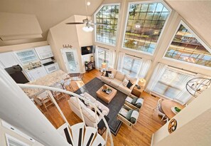 A spacious loft-style living area with a kitchen, large windows, and a staircase. - Peaceful Lakeside Escape with Dock & Hot Tub (Hot Springs)