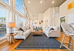 A spacious living room with a large window, a staircase, and a modern chandelier. - Peaceful Lakeside Escape with Dock & Hot Tub (Hot Springs)