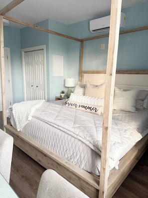 Un lit à baldaquin avec une couvre-lit matelassée, une lampe de chevet et un climatiseur fixé au mur.