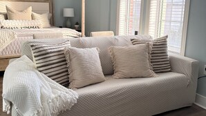 Un dormitorio con una cama, un sofá cama, una ventana con persianas y una mesita de noche con lámpara.