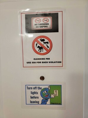 Eine Wand mit drei Schildern: eines verbietet Rauchen und Dampfen, ein weiteres warnt vor einer Reinigungsgebühr bei Verstößen und ein drittes weist an, das Licht auszuschalten, bevor man geht.