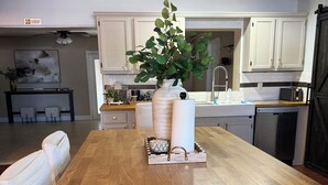 Une cuisine spacieuse avec des meubles blancs, une table à manger en bois et une plante en pot.