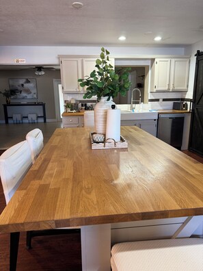 Een ruime keuken met witte kasten, een houten eettafel en een bloempot.