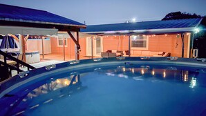 Une piscine dotée d’une terrasse couverte, d’un espace extérieur aménagé pour s’asseoir et d’un bâtiment avec un toit en pente.