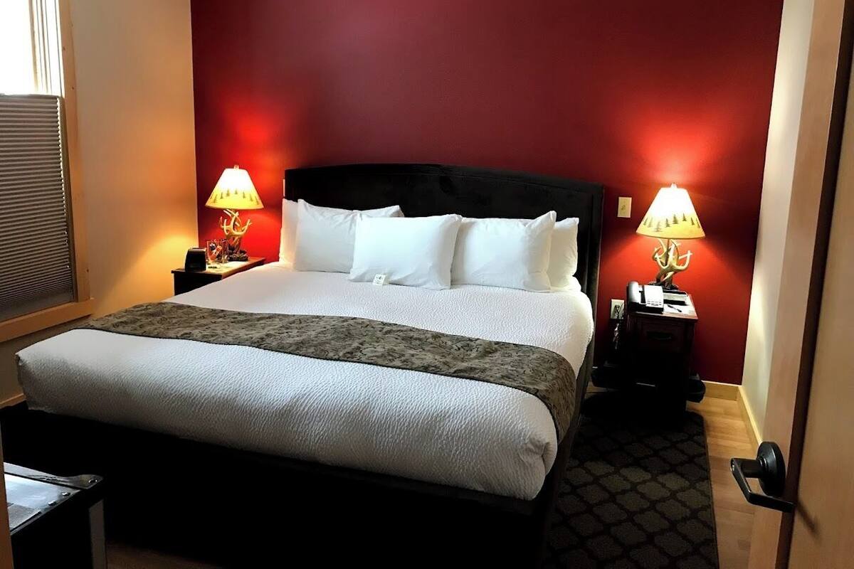 A hotel room with a large bed, two bedside tables with lamps, a red accent wall, and a patterned rug.