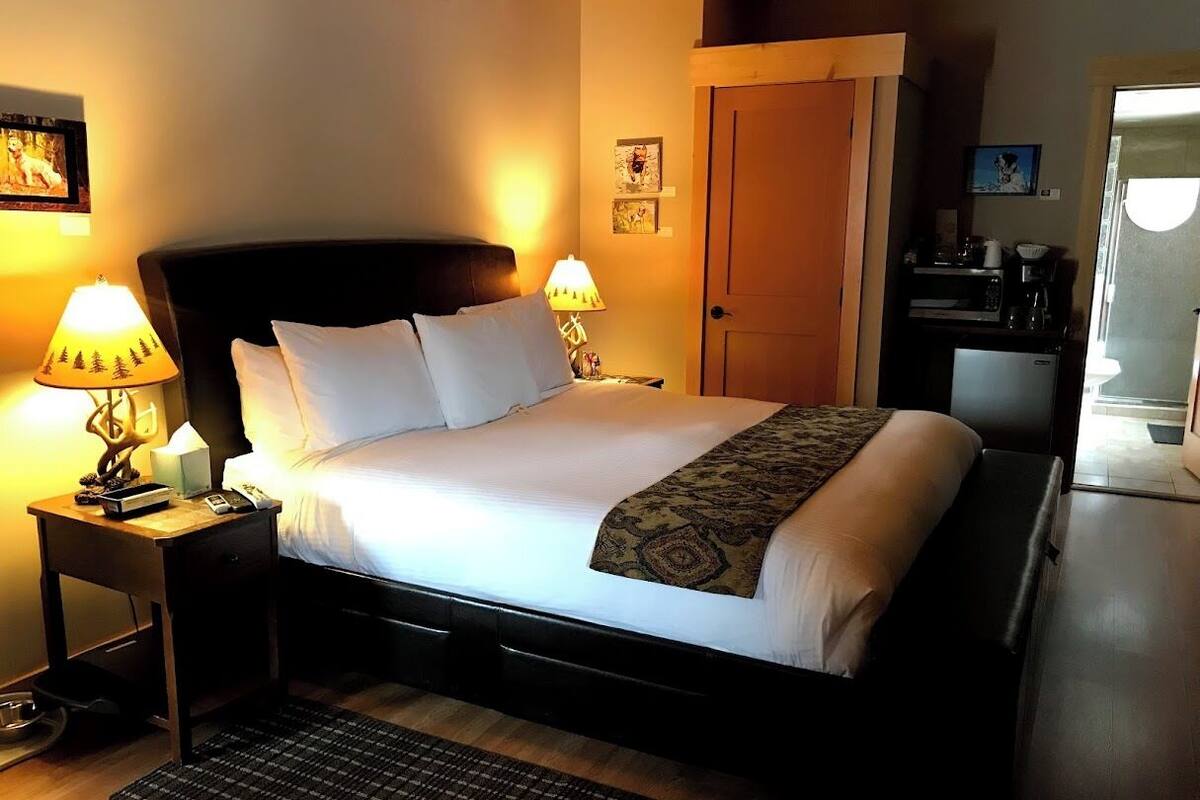 A neatly made bed with a headboard, two bedside lamps, a small bedside table, and a rug on a wooden floor.