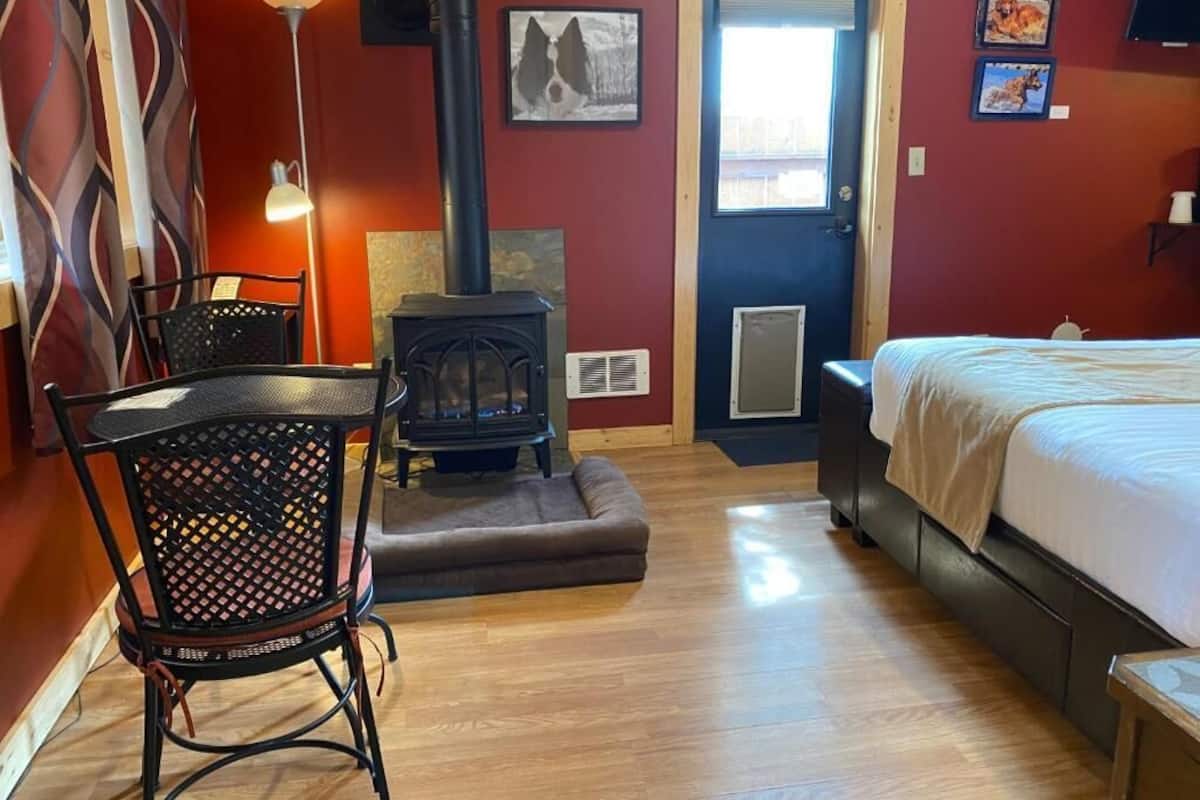 A cozy room with a bed, a chair, a table, a fireplace, and a door.