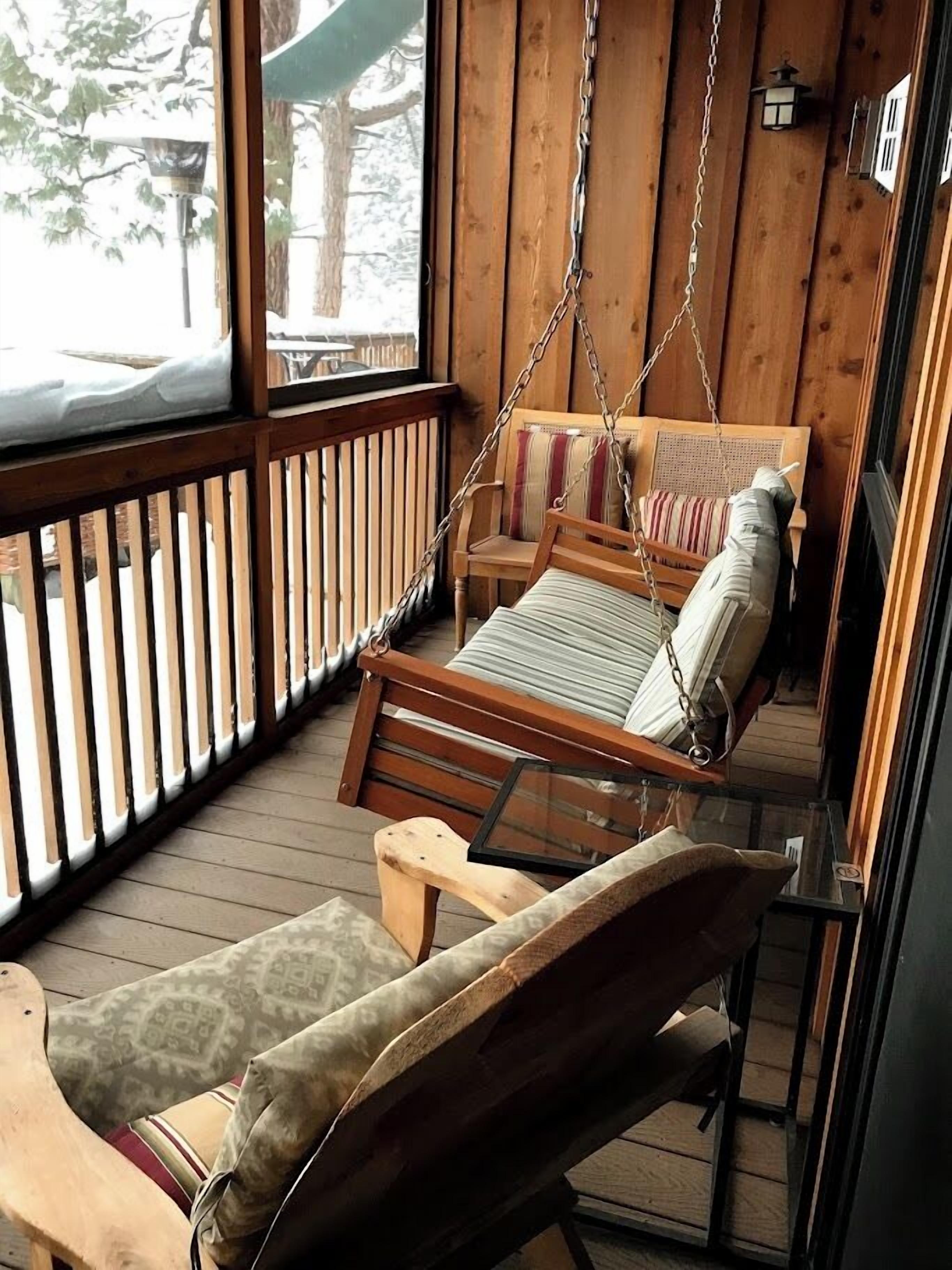 A wooden porch with a swing chair and a cushioned bench.
