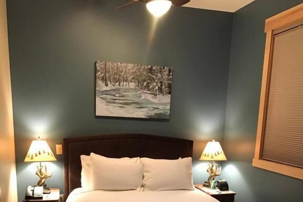 A neatly made bed with a headboard, two bedside tables with lamps, a ceiling fan, and a framed picture on the wall.